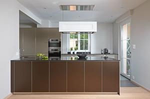 Die Einbauküche b3 von bulthaup besticht durch ihre zweifarbige Ausführung. Die Kücheninsel steht mit ihren bronzefarbenen Aluminiumfronten im Vordergrund, die lehmfarbene Hochschrankzeile nimmt sich dezent zurück. Kanten und Sockel der Küche sind in Aluminium gehalten. Eine hochglänzende Granitarbeitsplatte sorgt für spiegelnde Effekte. Die offene Wohnküche überzeugt mit harmonisch gestalteten Übergängen von Farben und Materialien. Hochwertige Einbaugeräte von Gaggenau und der höhenverstellbare und beleuchtbare Dunstabzug von Berbel sind weitere Highlights in diesem Küchentraum.