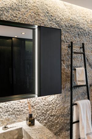 Das angrenzende Badezimmer ist durch das Spiel mit verschiedenen Naturmaterialien das Highlight der Wohnung. Als Raumteiler dient eine freistehende Badewanne, die mit schwarzem Naturstein einen Kontrast zum Holzboden bildet.