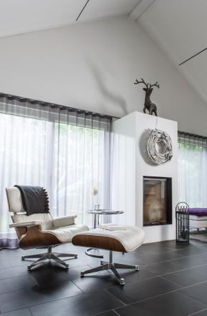 Über dem zwischen Sofa und Loungesessel (Lounge Chair, Design Charles und Ray Eames) platzierten Kaminblock thront ein kapitaler Hirsch und wirft seinen imposanten Schatten an die Wand.