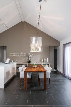 Der massive Esstisch mit weich gepolsterten Stühlen befindet sich unmittelbar neben dem Küchenblock. So kann die Bewohnerin jederzeit mit Gästen kommunizieren. Highlight: Kronleuchter Light Shade Shade.