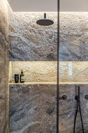 Das angrenzende Badezimmer ist durch das Spiel mit verschiedenen Naturmaterialien das Highlight der Wohnung. Als Raumteiler dient eine freistehende Badewanne, die mit schwarzem Naturstein einen Kontrast zum Holzboden bildet.