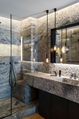 Das angrenzende Badezimmer ist durch das Spiel mit verschiedenen Naturmaterialien das Highlight der Wohnung. Als Raumteiler dient eine freistehende Badewanne, die mit schwarzem Naturstein einen Kontrast zum Holzboden bildet.