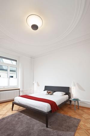 Das reduzierte Bett Theo, Lema, in Kombination mit den Beistelltischen Bella und den Leuchten I Cono (Wand) und Funnel (Decke) lässt den wunderschönen Altbau mit Stuckdecke wirken.